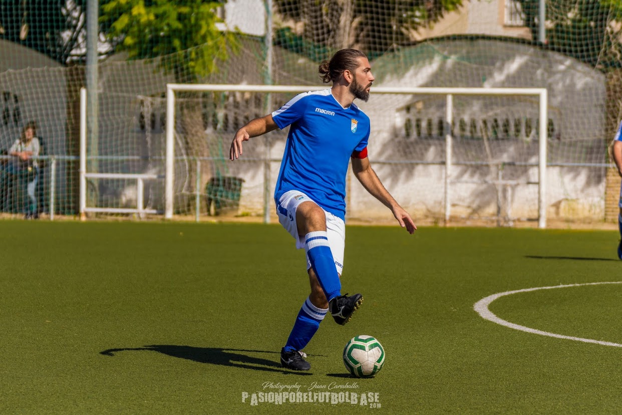 Antonio González skillfully controlling a football during a game on a sunny day, wearing a blue jersey, with a focused expression as he prepares to make his next move on the field.