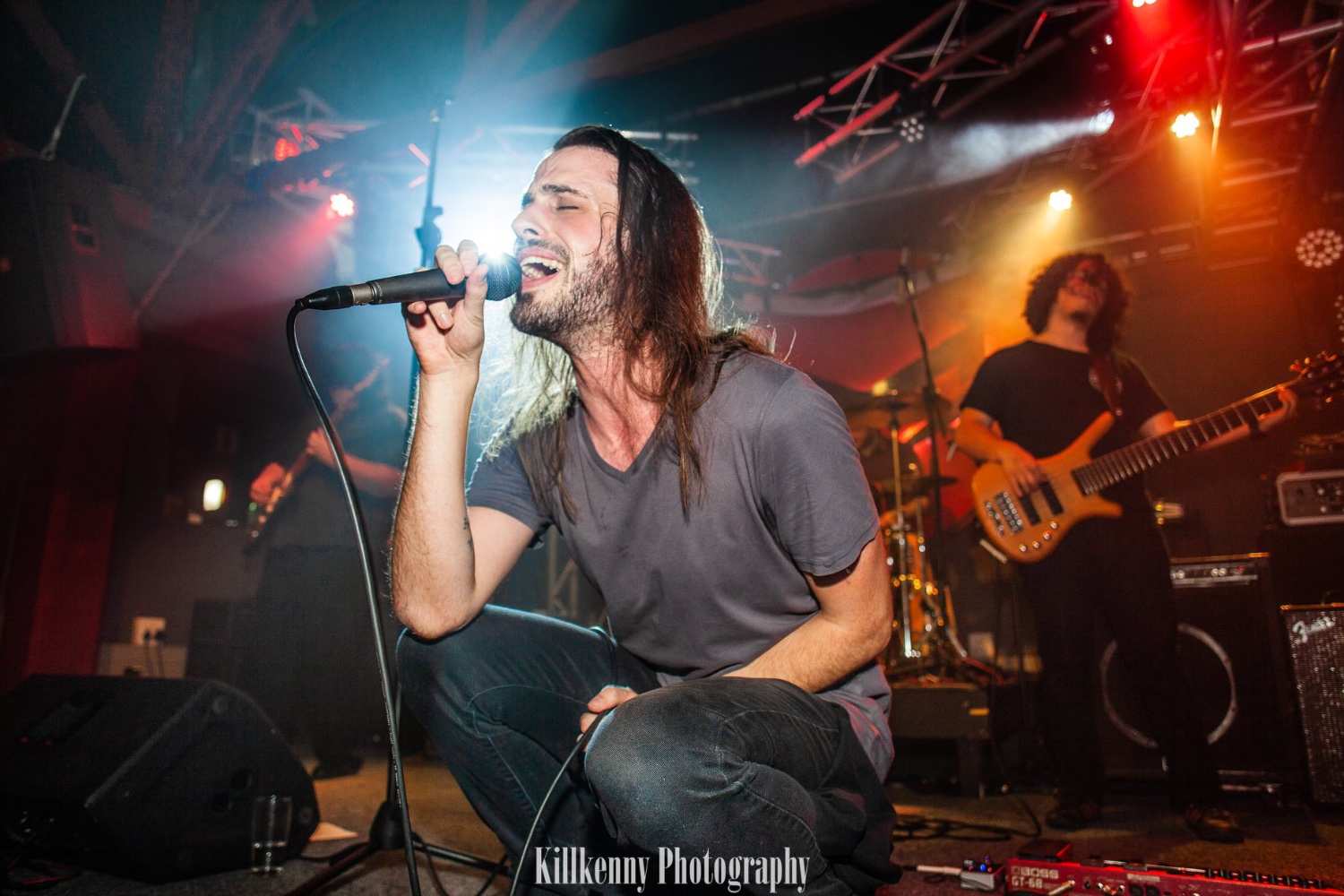 Clem van der Merwe passionately performing as the lead vocalist on stage with his band, Black Moscow, captured mid-song, with vibrant stage lighting and a bassist playing in the background.